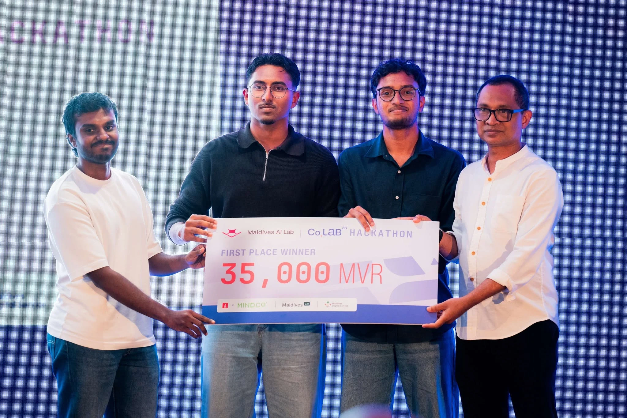 Team members holding the first-place winner board at the 2026 BML × MINDCo hackathon.